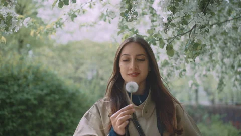 Young female blowing into dandelion while looking into the camera Stock Footage 203585566