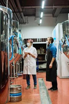 Young female brewery expert in whitecoat and protective mask and male brewer Stock Photos