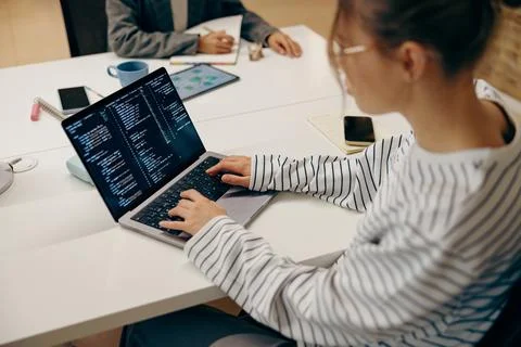 Young female computer programmer is coding at laptops while sitting in coworking Stock Photos