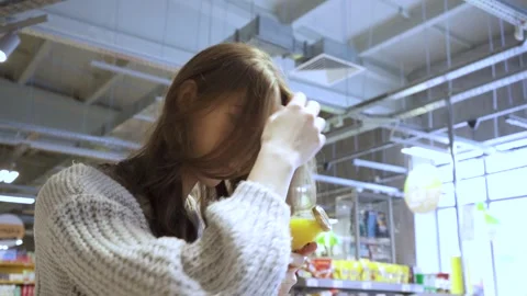 A young female customer reads the composition of the drink on the juice bottle Stock Footage 169746587