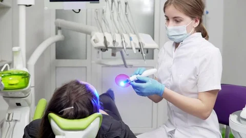 Young female dentist in mask and gloves using dental UV light equipment for Stock Footage