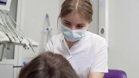 Young Female Dentist in Mask approaching With Tools. Dental Lamp Lights Into a Stock Footage