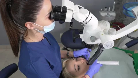 Young female dentist treating root canals using microscope at dental clinic. Vidéo 239729232