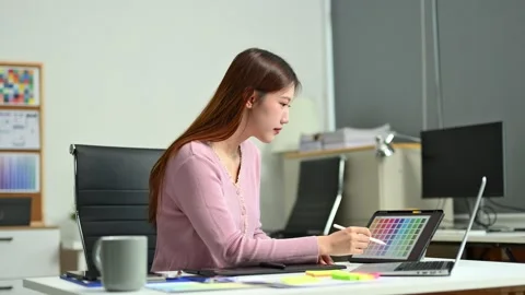 Young female designer using digital tablet and laptop in a modern creative .. Video stock 312437035