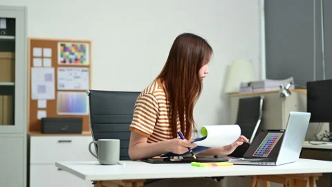 Young female designer using digital tablet and laptop in a modern creative .. Video stock 312437152