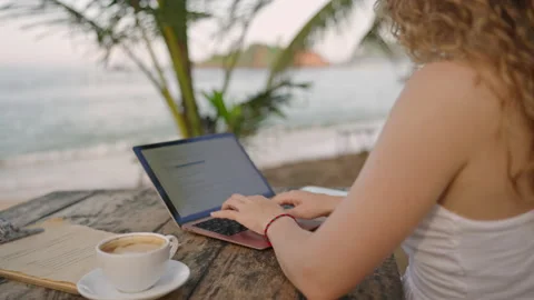 Young female developer working on laptop by the ocean. Woman freelancer coding Stock Footage 234431109
