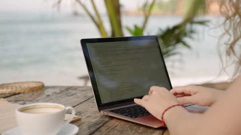 Young female developer working on laptop by the ocean. Woman freelancer coding Stock Footage 239412125