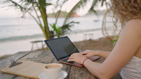 Young female developer working on laptop by the ocean. Woman freelancer coding Stock Footage 241523746