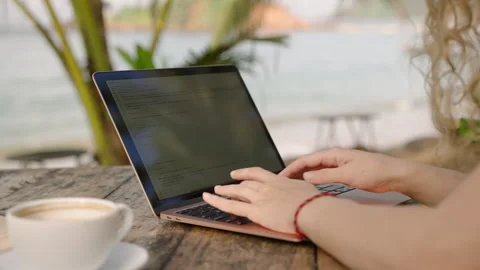 Young female developer working on laptop by the ocean. Woman freelancer coding Stock Footage 241524183