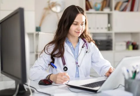 Young female doctor trainee making important notes for work, sitting at the Stock Photos