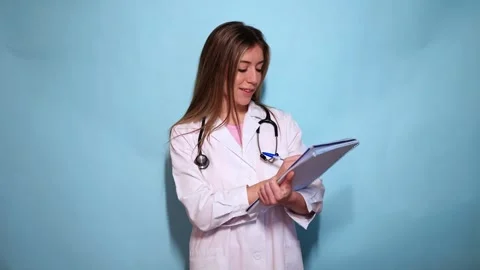Young female doctor writing notes on a clipboard on a blue background Stock Footage 297675201