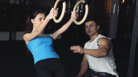 Young female doing ring row with her male trainer slow motion Stock Footage 61292343