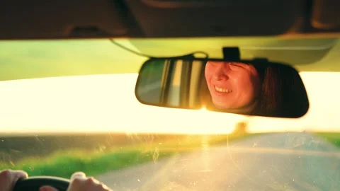 Young female driver reflected in rearview mirror. Car trip on vacation, smiling Stock Footage 335490732