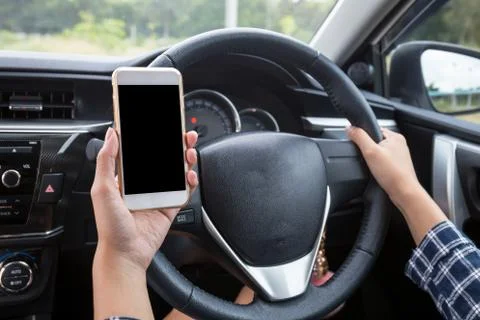 Young female driver using touch screen smartphone and hand holding steering w Stock Photos