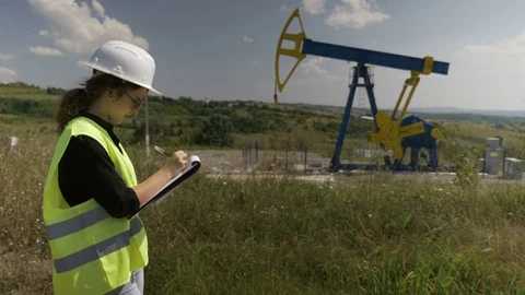 Young female engineer doing research near an oil pump unit noting information Stock Footage 82179015