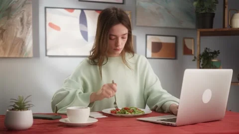 Young female freelancer working or chatting on laptop while eating fresh salad Stock Footage 150110108