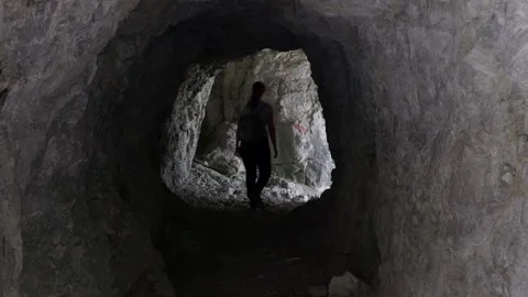 Young female hiker with a backpack exploring a dark, narrow rocky tunnel Stock-Footage 336942018