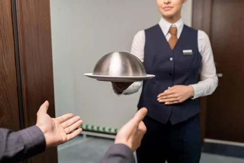 Young female hotel manager passing tray with breakfast to guest while standing Stock Photos