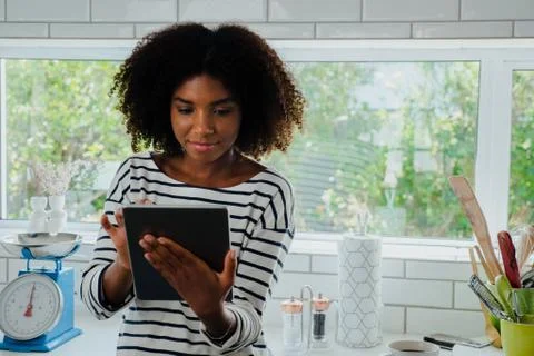 Young female in the kitchen browsing tablet for recipe, copy space Stock Photos