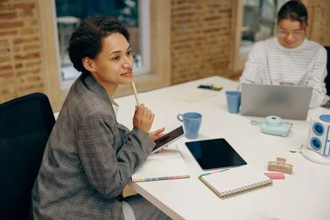 Young female manager is making notes while working on digital tablet sitting in Stock Photos