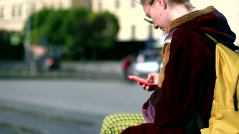 Young female person using smart phone mobile sitting on sunny city street. Onlin Stock Footage 131017456