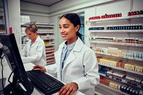 Young female pharmacist using computer with senior colleague using digital Stock Photos