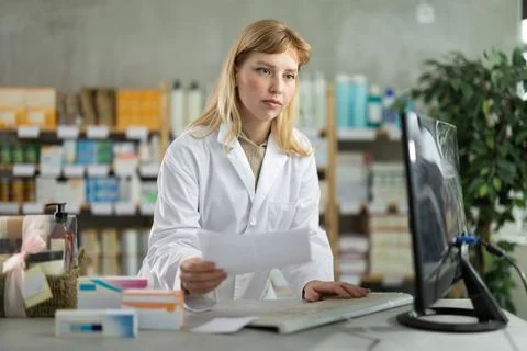 Young female pharmacist working with computer in chemists shop Stock Photos