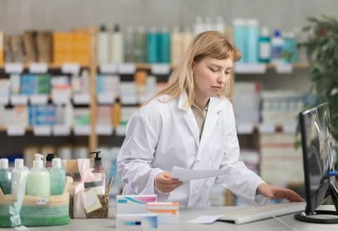 Young female pharmacist working with computer in chemists shop Stock Photos