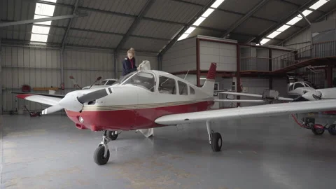 Young female pilot discovering light aircraft with protective cover in hangar Stock Footage 146376350
