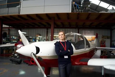 Young female pilot posing in front of her plane inside the hangar. Stock Photos