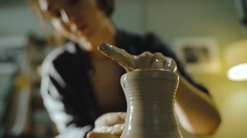 Young female potter gently pulls the walls of a clay vessel on a potter's wheel Stock Footage 202166353