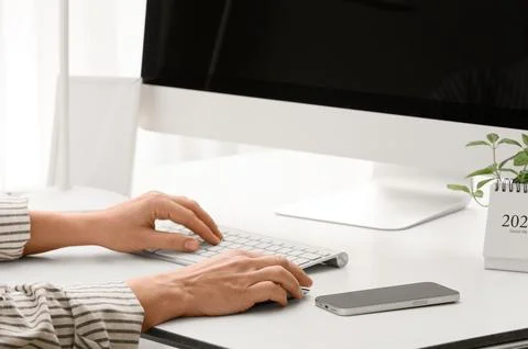 Young female programmer with computer and mobile phone typing on keyboard in  Stock Photos