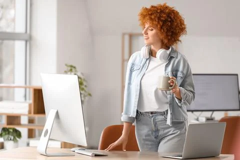 Young female programmer with cup of coffee near her workspace in office Stock Photos