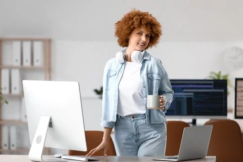 Young female programmer with cup of coffee near her workspace in office Stock-Fotos