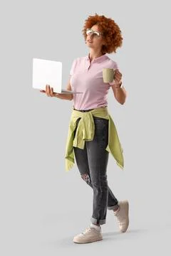 Young female programmer with laptop and cup of coffee on grey background Stock Photos