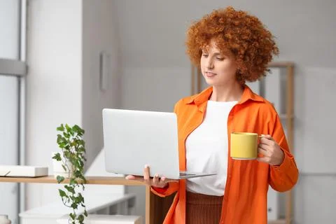 Young female programmer with laptop and cup of coffee in light office Stock-Fotos
