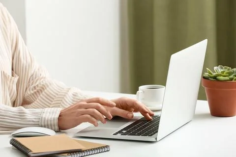 Young female programmer with laptop, cup of coffee and notebooks working in o 스톡 사진