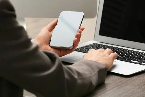 Young female programmer with mobile phone and laptop working in office, close Stock Photos