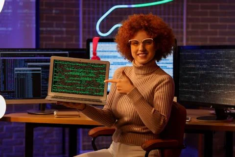 Young female programmer pointing at modern laptop in office at night Stock-Fotos