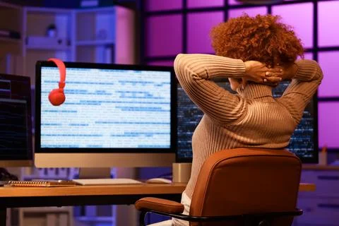 Young female programmer resting at her workspace in office at night, back vie Stock Photos