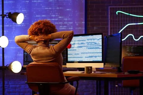 Young female programmer resting at her workspace in office at night, back vie Stock Photos