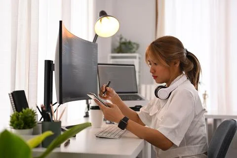 Young female programmer sitting front of computers with coded data on screen and Stockfoto's
