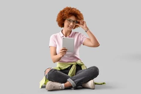 Young female programmer with tablet computer sitting on grey background Stock Photos