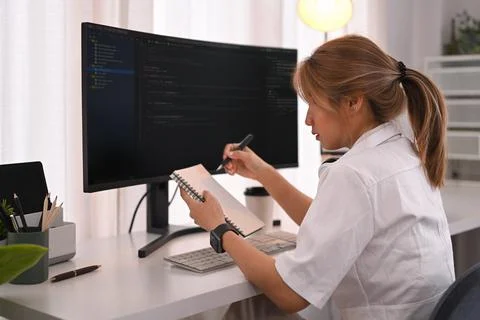 Young female programmer working with coded data on desktop computer in bright Stock Photos