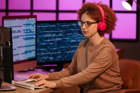 Young female programmer working with computer and headphones in office at nig Foto stock