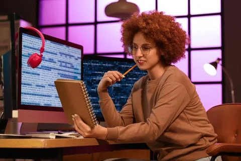 Young female programmer working with computer and notebook in office at night Stock Photos