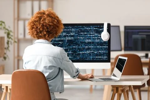 Young female programmer working with laptop and computer in office, back view 스톡 사진