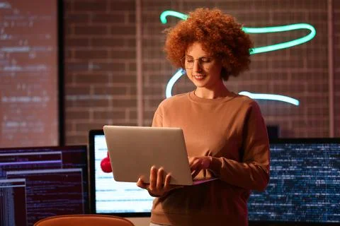 Young female programmer working with modern laptop in office at night Stock Photos