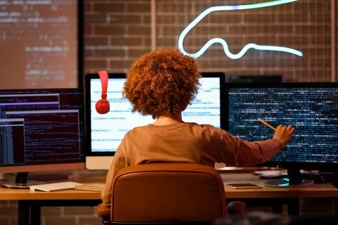 Young female programmer working with modern computer in office at night, back 스톡 사진