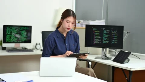 Young female programmer working with tablet and screen displaying code. Mod.. Stock Footage 312438181
